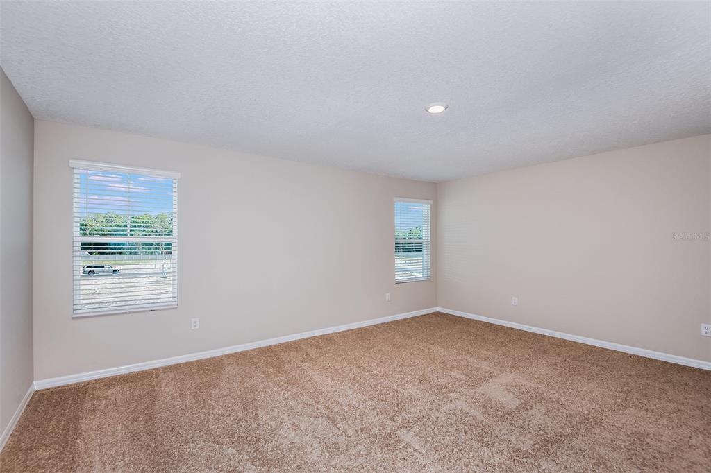An empty bedroom features beige walls, tan carpeting, and two windows with white blinds — 36613 SAGEMOOR DRIVE, ZEPHYRHILLS, FL