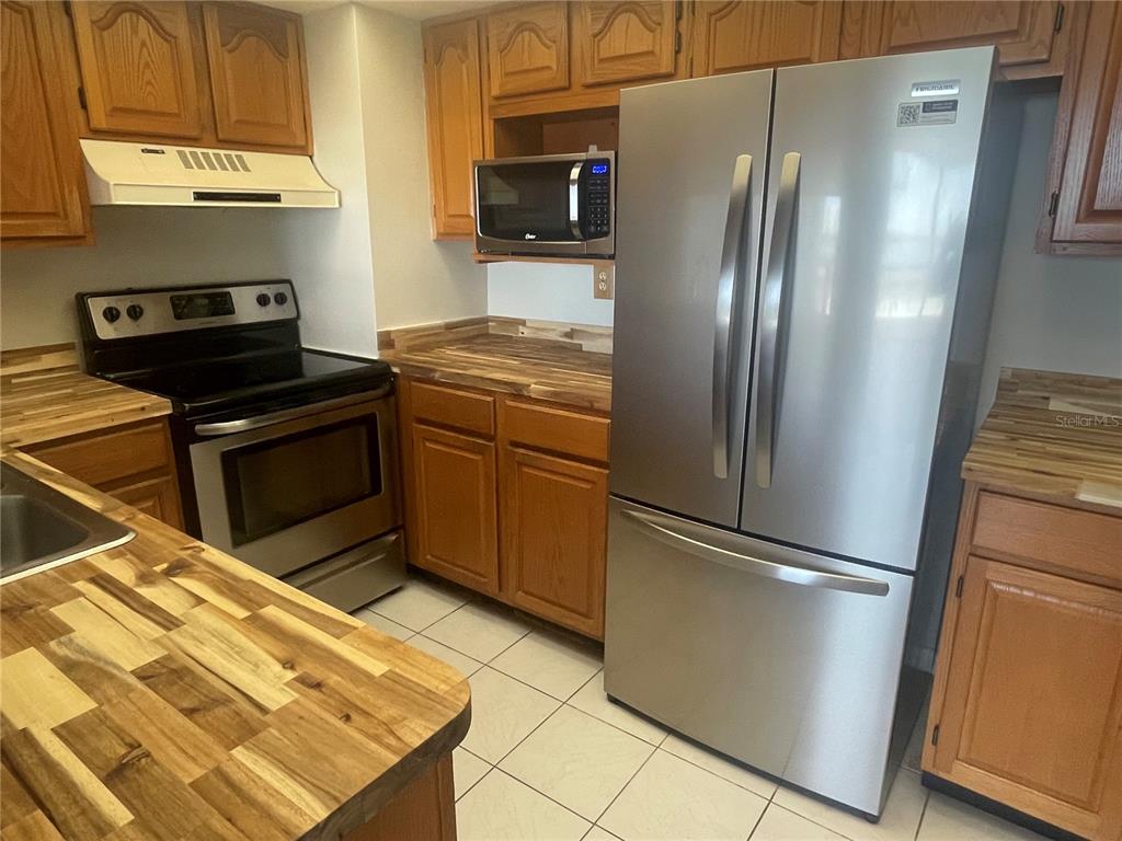 A kitchen features wood cabinets, butcher block countertops, stainless steel appliances, and white tile flooring — 400 ISLAND WAY UNIT 908, CLEARWATER BEACH, FL