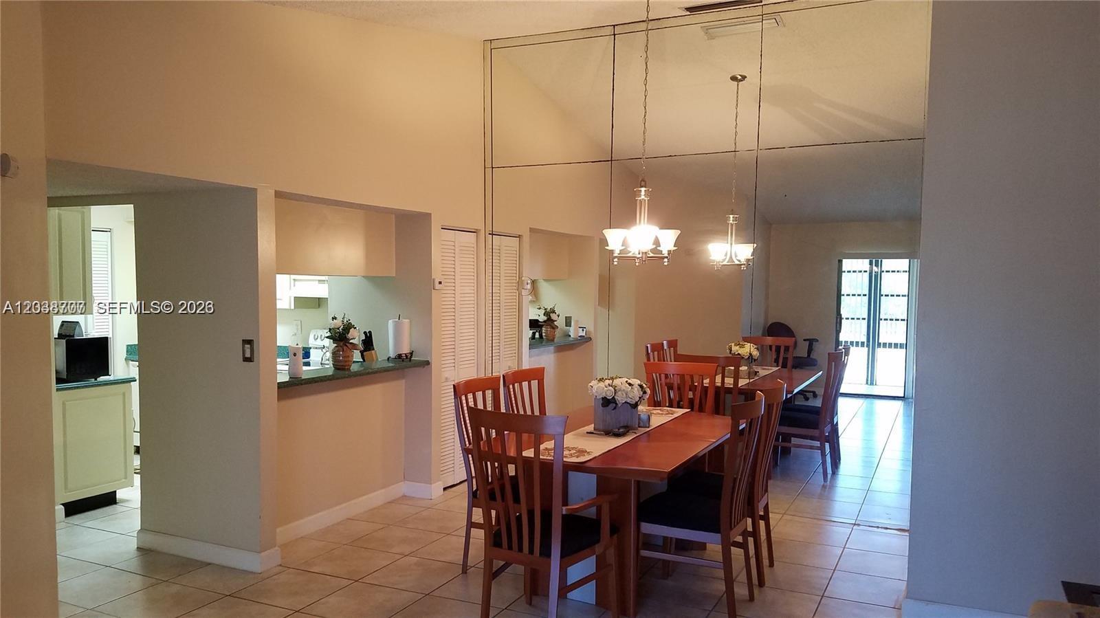 A dining room with a wooden table, chairs, mirrored wall, and an adjacent kitchen — 931 NE 199th St # 22, Miami FL 33179, MIAMI, FL
