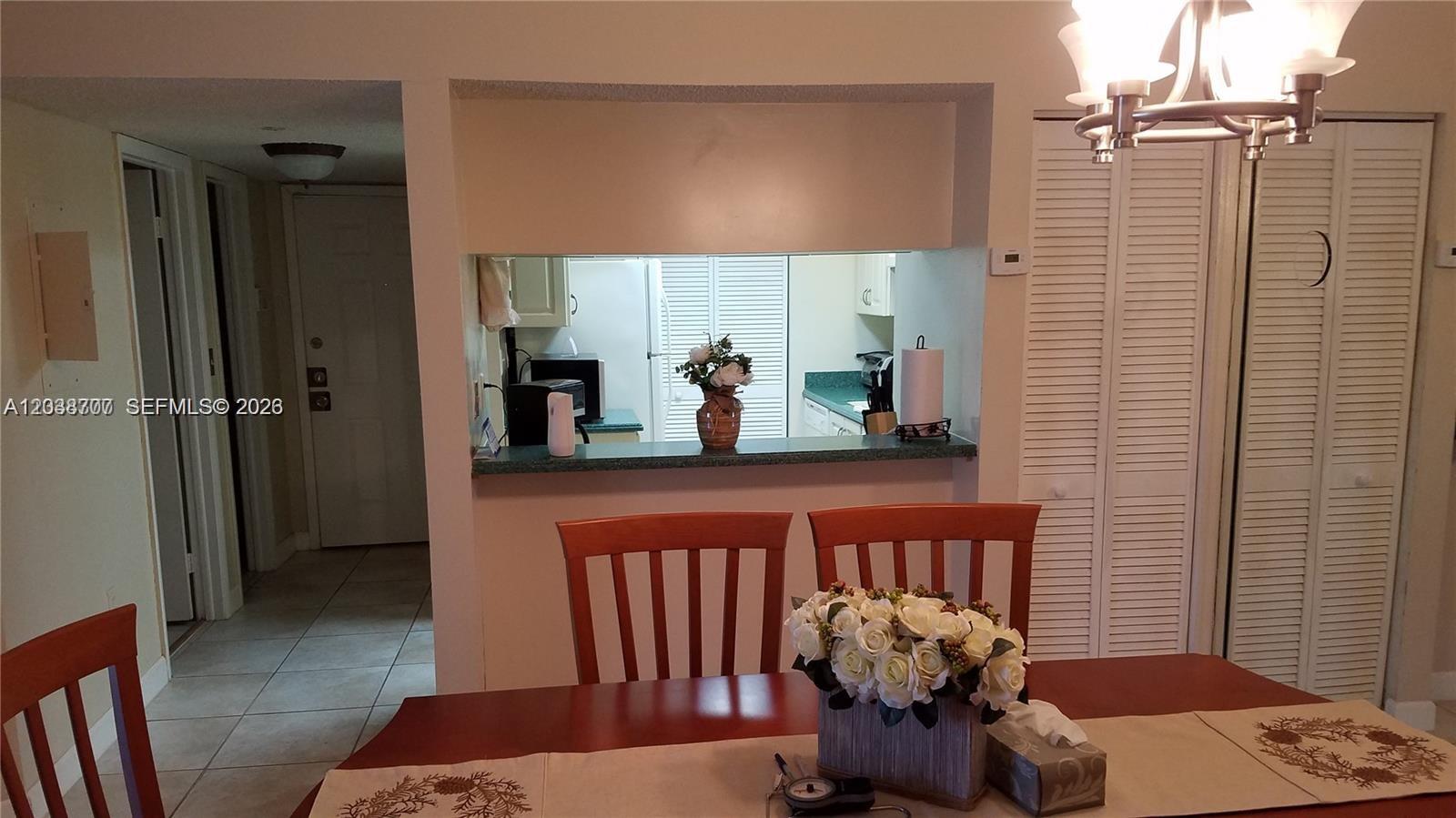 A dining area with a wooden table and chairs looks through a pass-through window into a kitchen — 931 NE 199th St # 22, Miami FL 33179, MIAMI, FL