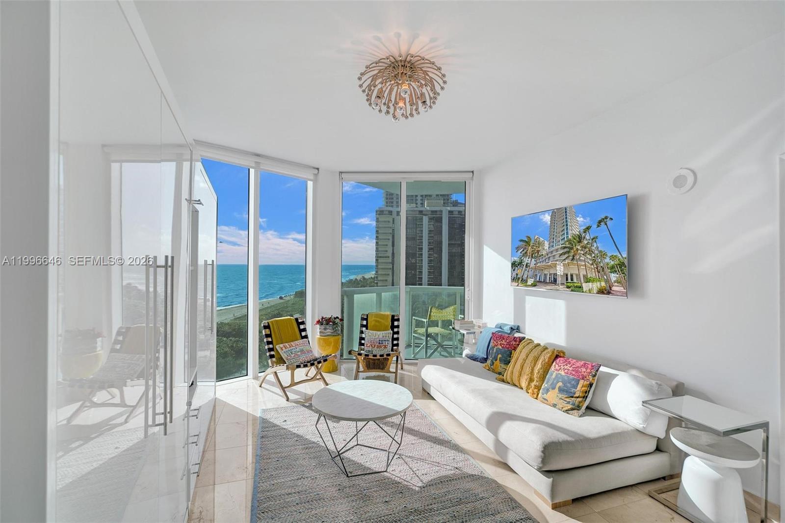 A modern living room features floor-to-ceiling windows with ocean views and a white sofa — 6515 Collins Ave # 804, Miami Beach FL 33141, MIAMI BEACH, FL