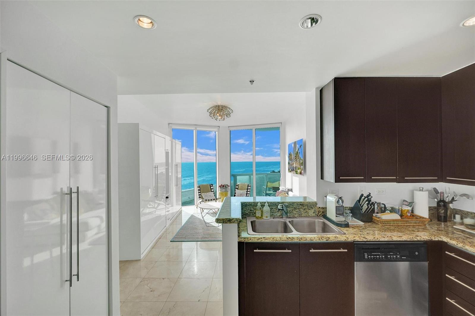 A kitchen with dark cabinets and granite countertops overlooks a living area with ocean views — 6515 Collins Ave # 804, Miami Beach FL 33141, MIAMI BEACH, FL