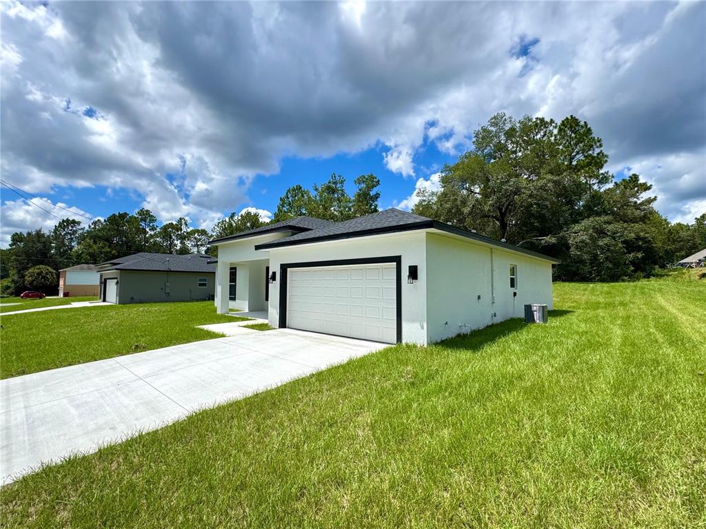 A white single-story house with a two-car garage and a concrete driveway under a cloudy sky — 8050 N OBERON TERRACE, DUNNELLON, FL