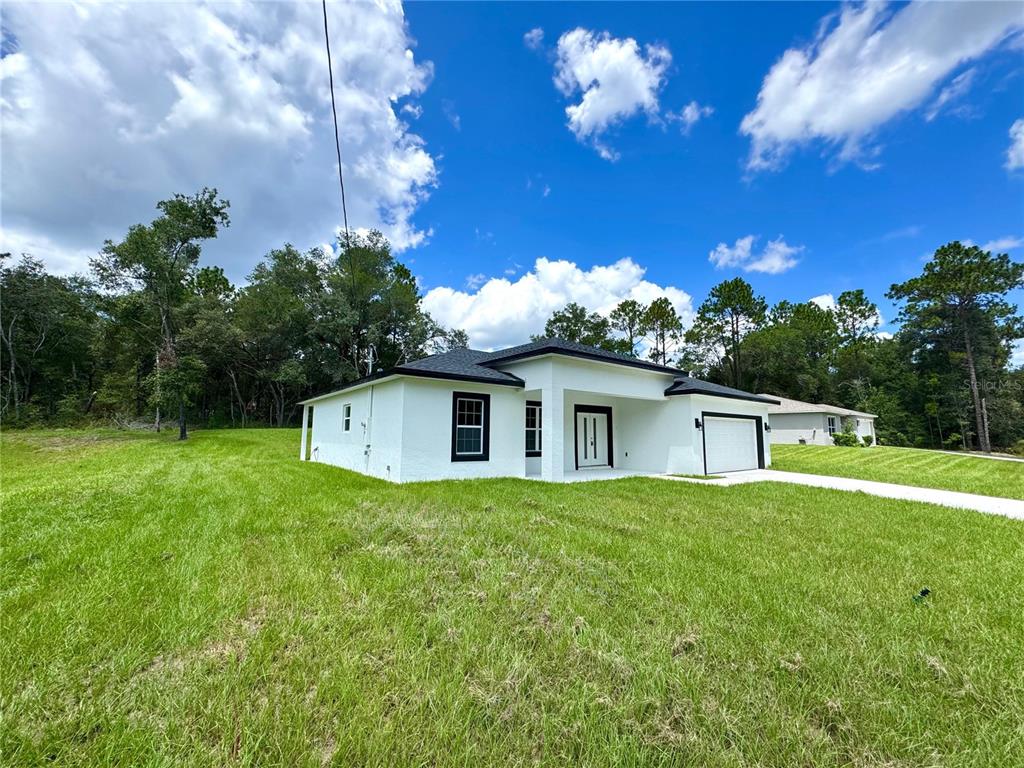 A white single-story house with a black roof and black window frames sits on a lawn — 8050 N OBERON TERRACE, DUNNELLON, FL