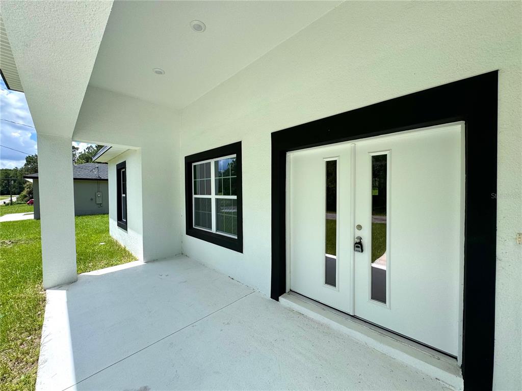 A white house exterior features a covered porch, a window, and a double front door — 8050 N OBERON TERRACE, DUNNELLON, FL