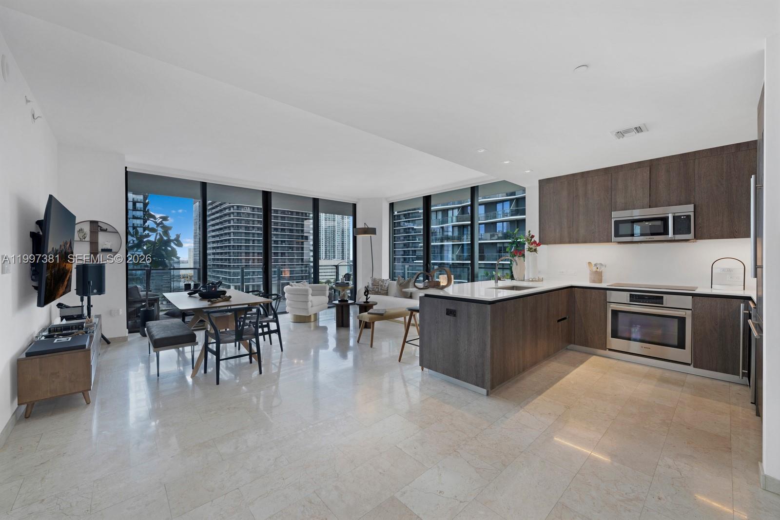A modern open-concept living and dining area features floor-to-ceiling windows and a sleek kitchen — 88 SW 7th St # 1401, Miami FL 33130, MIAMI, FL