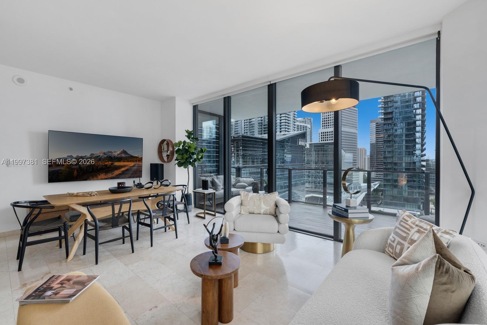 A modern living and dining area features floor-to-ceiling windows overlooking a dense city skyline — 88 SW 7th St # 1401, Miami FL 33130, MIAMI, FL