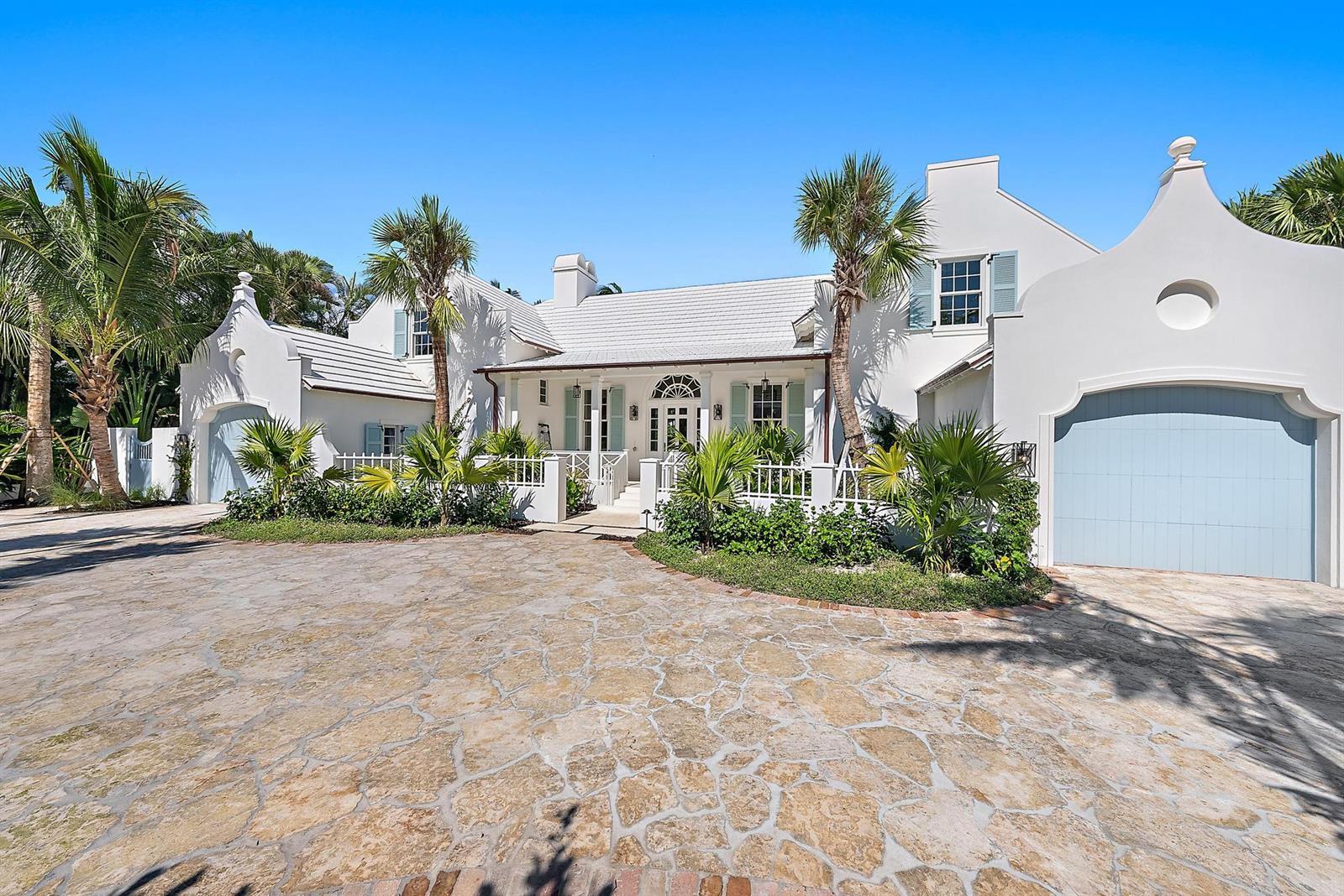 A white house with a stone driveway, blue garage doors, and palm trees under blue sky — 269 Jamaica Lane, Palm Beach FL 33480, PALM BEACH, FL
