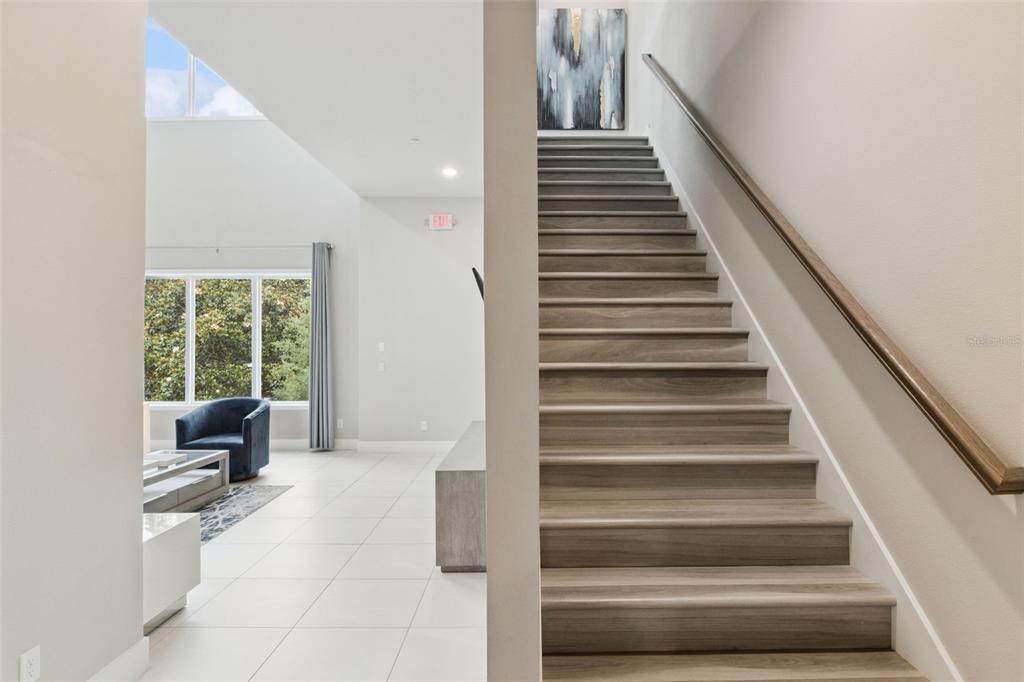 A staircase with wood-look treads leads upward next to a bright, open-concept living area — 7760 SANDY RIDGE DRIVE UNIT 214, REUNION, FL
