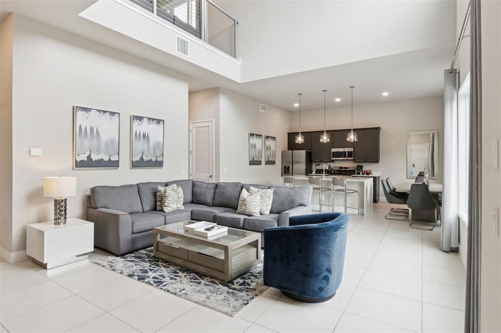 A modern open-concept living room and kitchen featuring a grey sectional, blue armchair, and island — 7760 SANDY RIDGE DRIVE UNIT 214, REUNION, FL