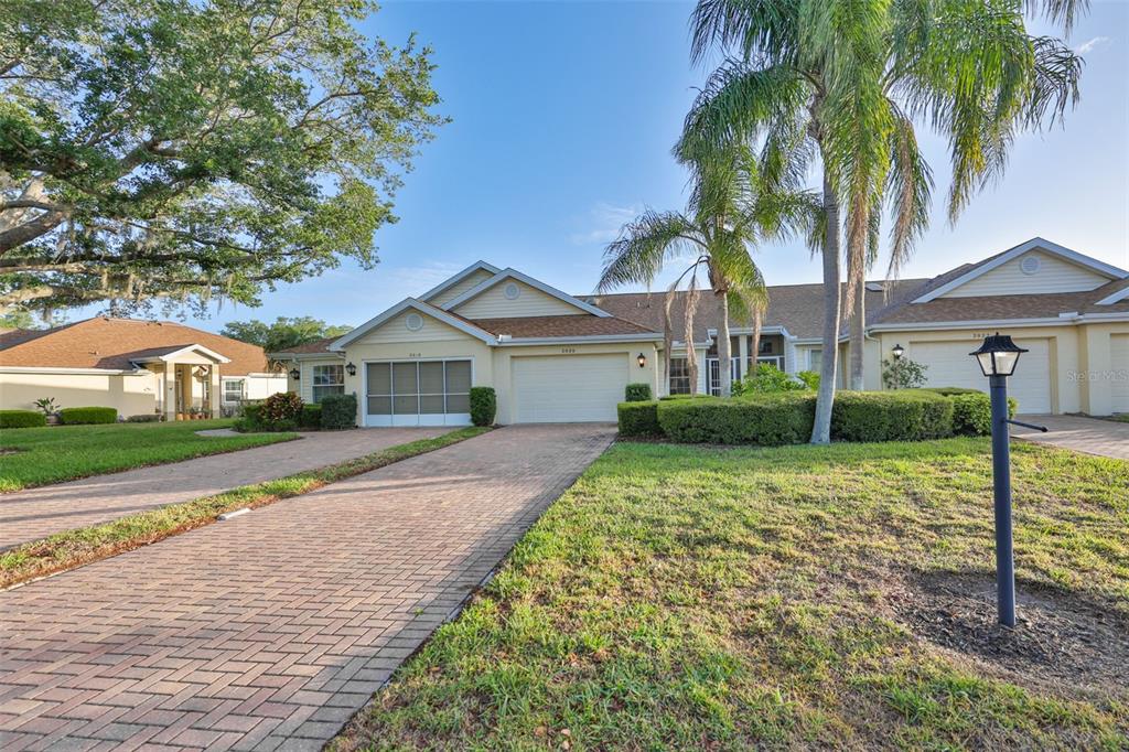 A view of a tan single-story house with a brick driveway and a palm tree — 2020 NANTUCKET DRIVE, SUN CITY CENTER, FL