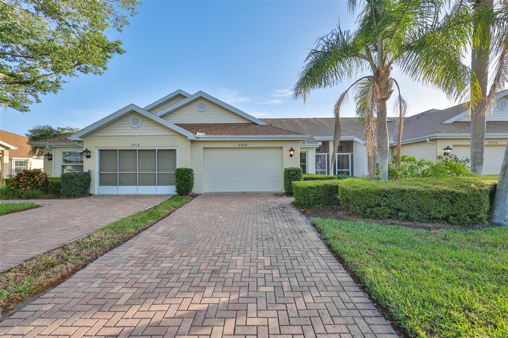 A beige duplex with a paver driveway, a two-car garage, and a palm tree — 2020 NANTUCKET DRIVE, SUN CITY CENTER, FL