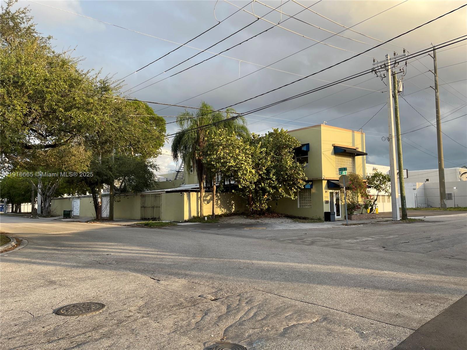 A two-story light-colored building stands at a street corner with trees and utility poles — 2299 NW 25th Ave, Miami FL 33142, MIAMI, FL