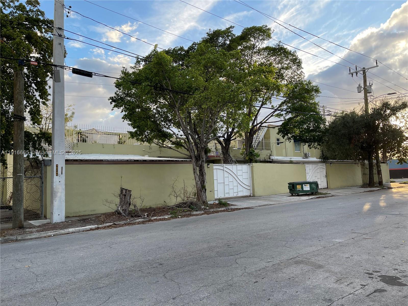 A street-level view shows a light green stucco wall with white gates and large trees — 2299 NW 25th Ave, Miami FL 33142, MIAMI, FL