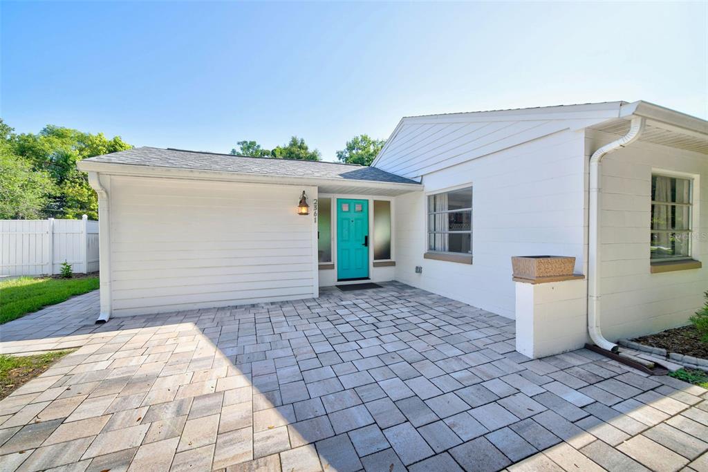 A white house exterior features a bright teal front door and a paved stone patio — 2361 ROXBURY ROAD, WINTER PARK, FL