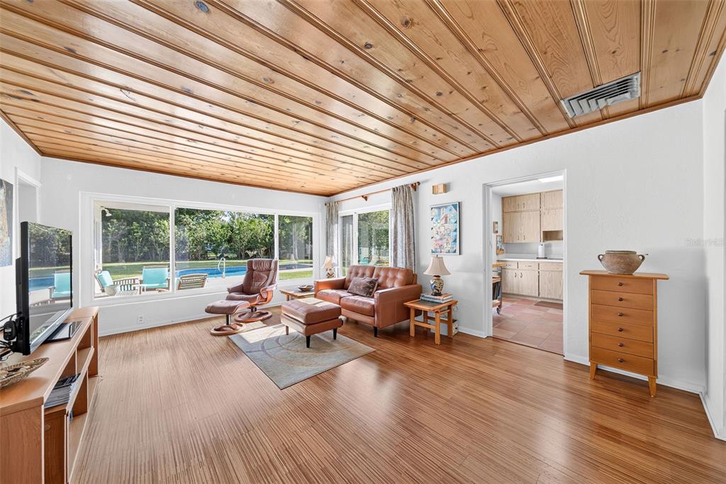A living room features wood-paneled ceilings, hardwood floors, and a large window overlooking a pool — 2361 ROXBURY ROAD, WINTER PARK, FL