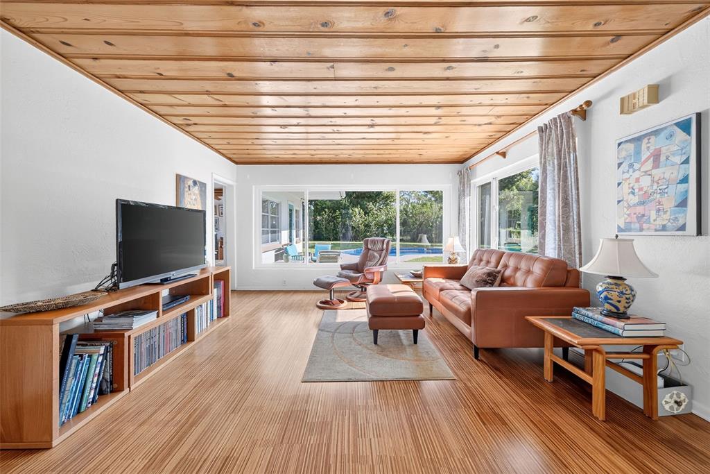 A living room features a wood-paneled ceiling, striped hardwood floors, and a view of a pool — 2361 ROXBURY ROAD, WINTER PARK, FL