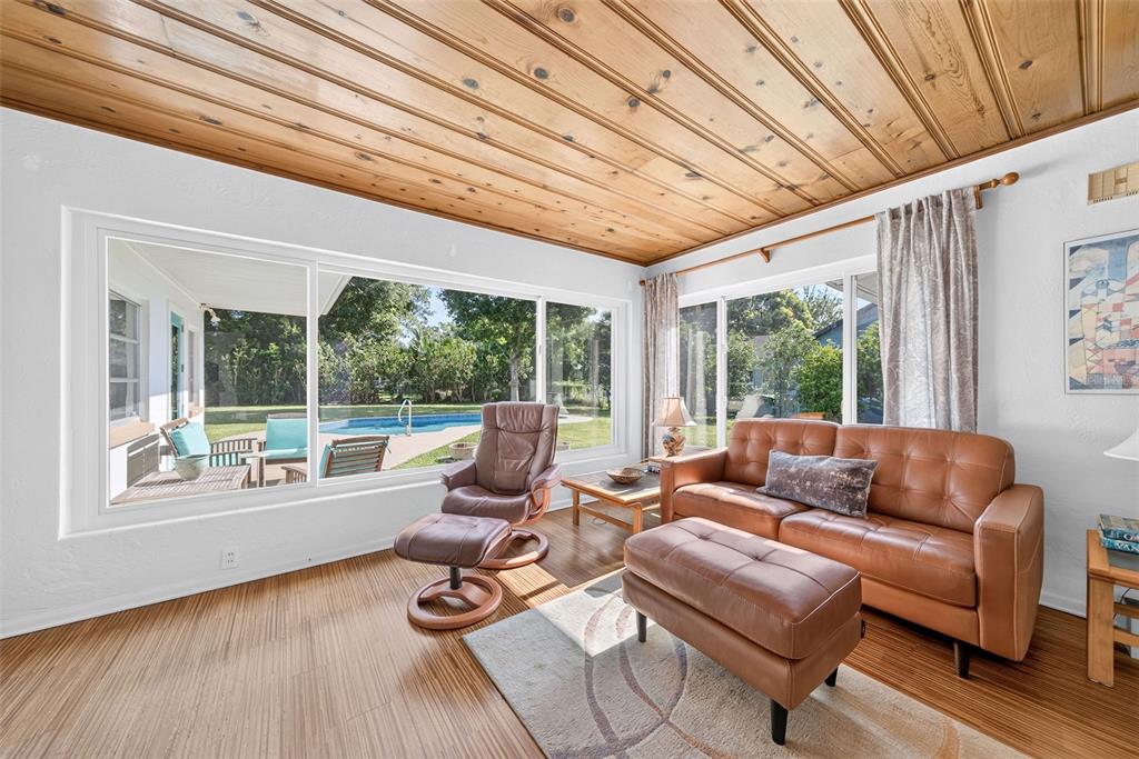 A living room with wood-paneled ceilings, a leather sofa, and large windows overlooking a pool — 2361 ROXBURY ROAD, WINTER PARK, FL