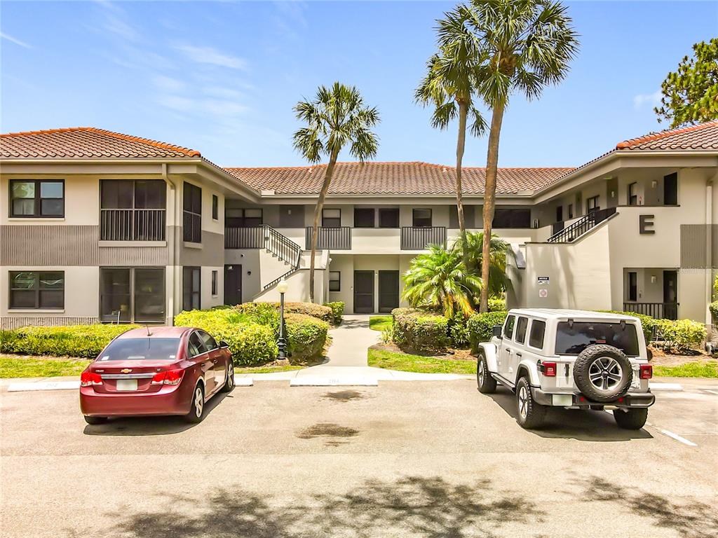 A two-story apartment building exterior with a parking lot, two cars, and palm trees — 2650 COUNTRYSIDE BOULEVARD UNIT E103, CLEARWATER, FL