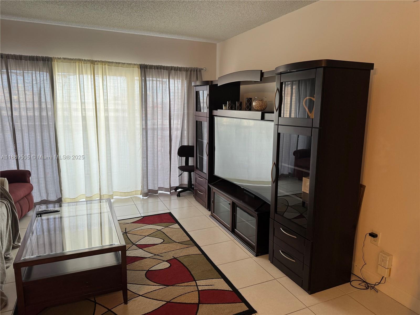 A living room features a large dark wood entertainment center, a glass coffee table, and curtains — 1985 S Ocean Dr # 15A, Hallandale Beach FL 33009, HALLANDALE BEACH, FL