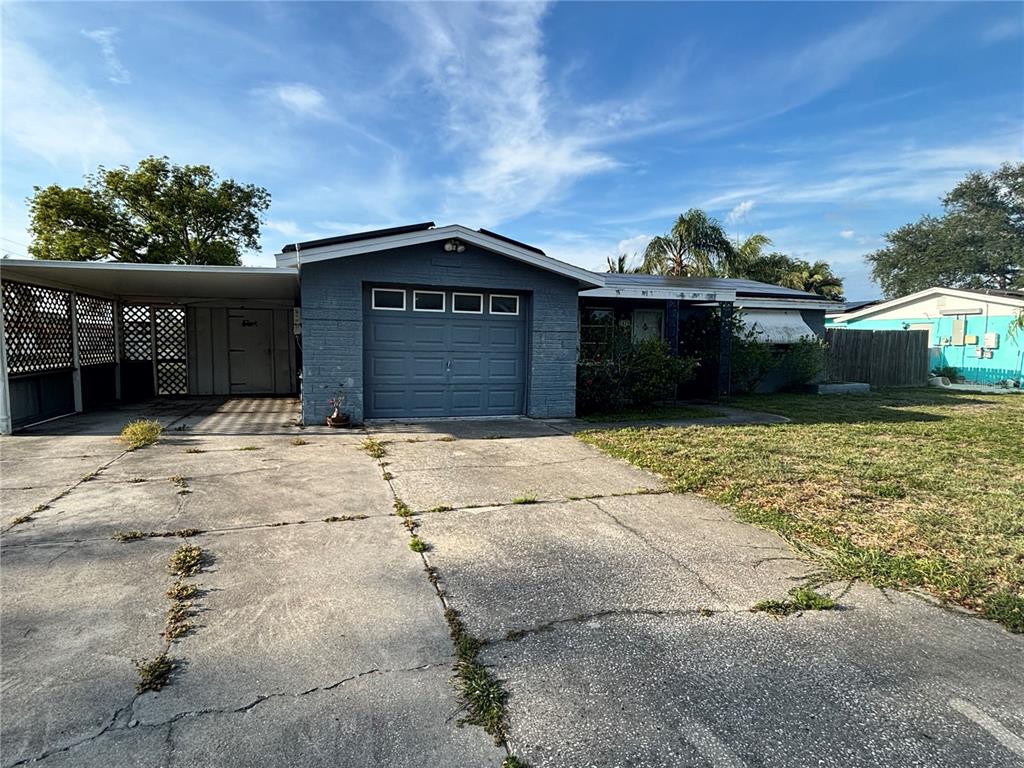 A single-story gray brick house features a garage, a carport, and a cracked concrete driveway — 3415 COLDWELL DRIVE, HOLIDAY, FL