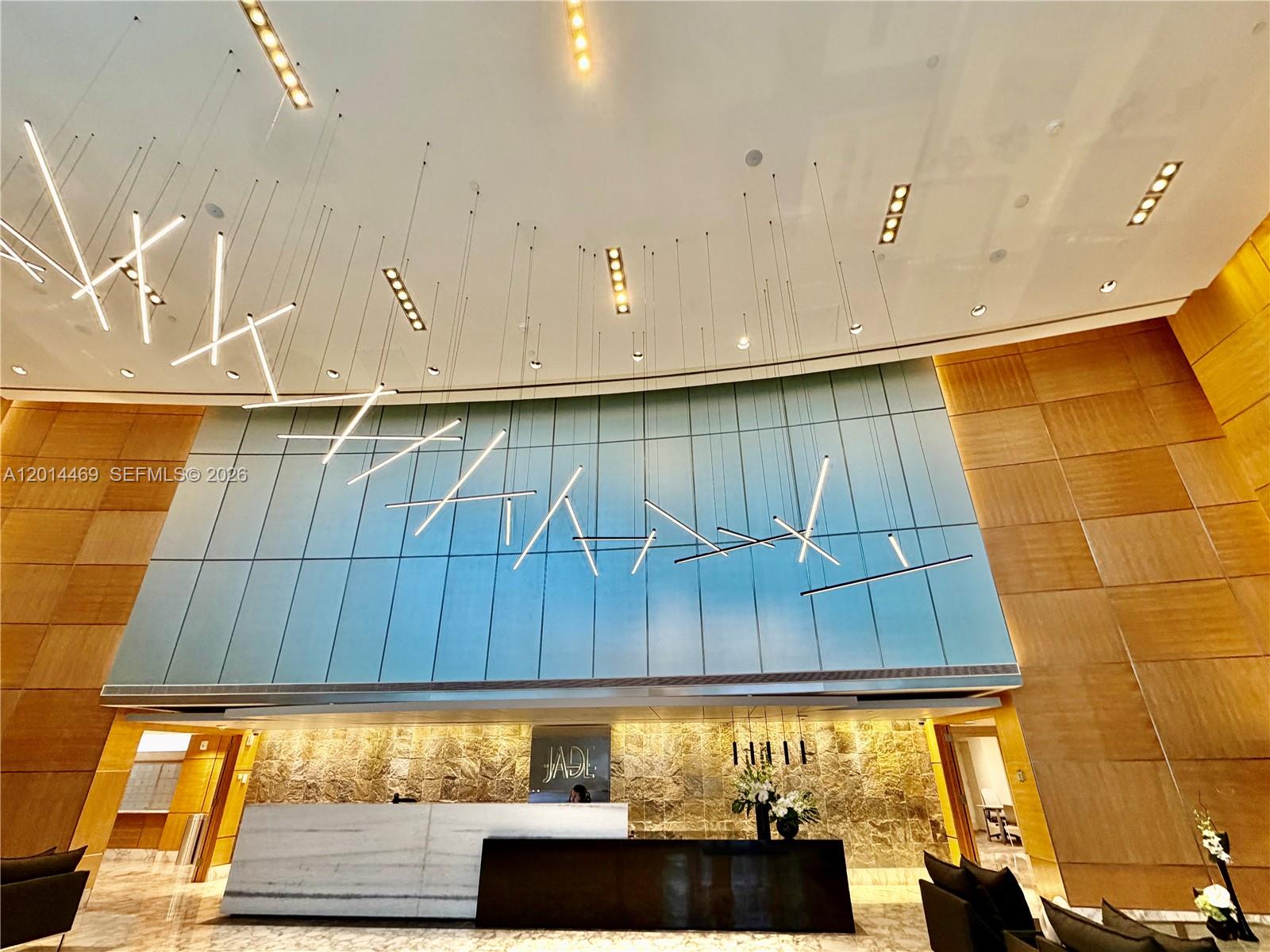 A modern building lobby features a stone reception desk, wood paneling, and hanging light fixtures — 1331 Brickell Bay Dr # 1006, Miami FL 33131, MIAMI, FL