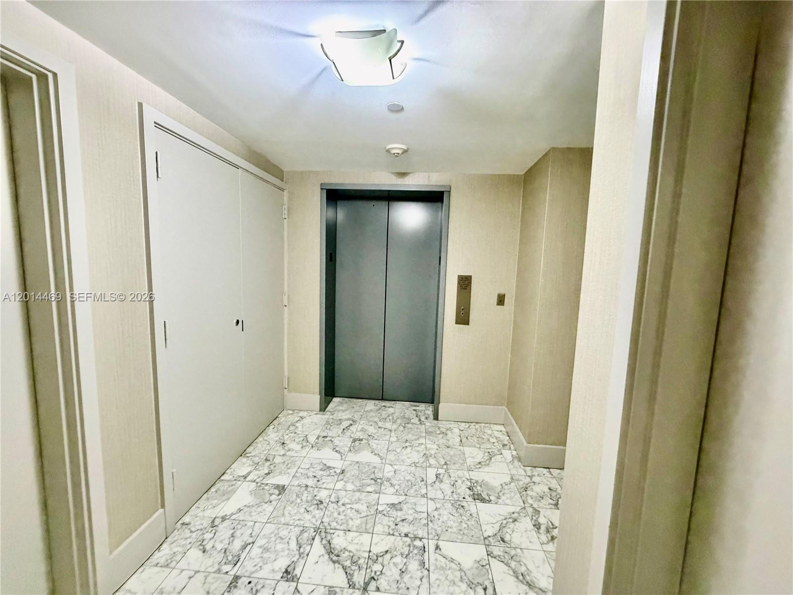 An elevator lobby features marble tile flooring, beige textured walls, and a white ceiling light — 1331 Brickell Bay Dr # 1006, Miami FL 33131, MIAMI, FL