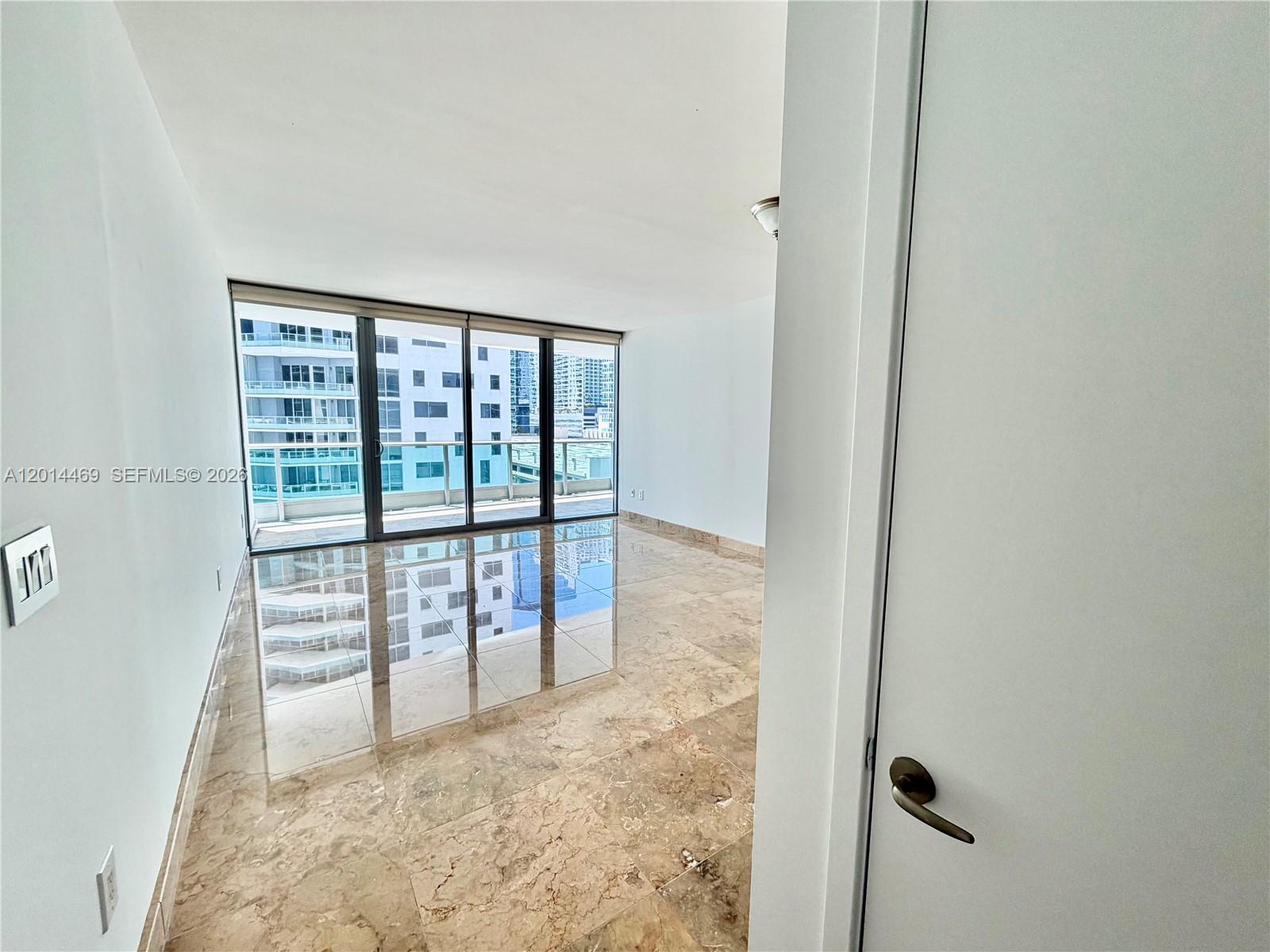 An empty room features polished marble floors, white walls, and floor-to-ceiling windows with balcony access — 1331 Brickell Bay Dr # 1006, Miami FL 33131, MIAMI, FL