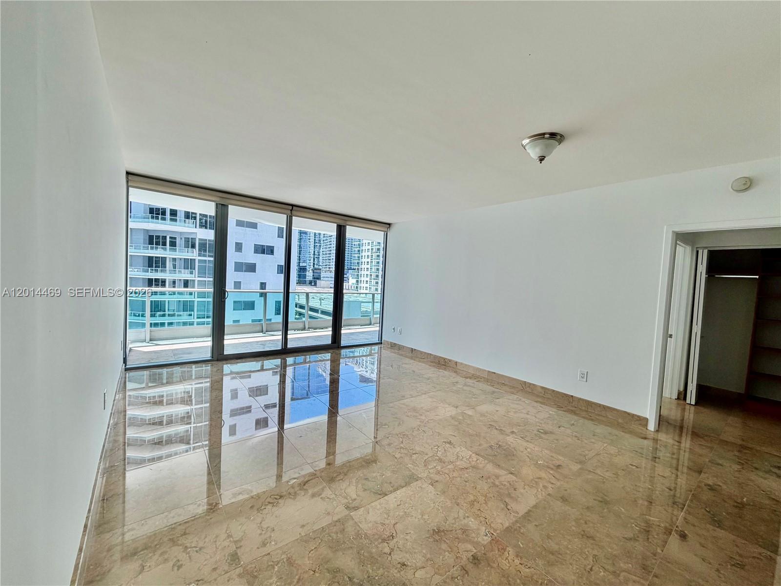 An empty room features polished marble floors, white walls, and floor-to-ceiling windows overlooking city buildings — 1331 Brickell Bay Dr # 1006, Miami FL 33131, MIAMI, FL