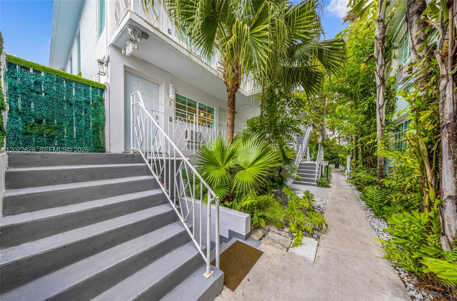 Exterior view of a multi-story apartment building with stairs, lush landscaping, and a walkway — 7830 Abbott Ave # 25, Miami Beach FL 33141, MIAMI BEACH, FL