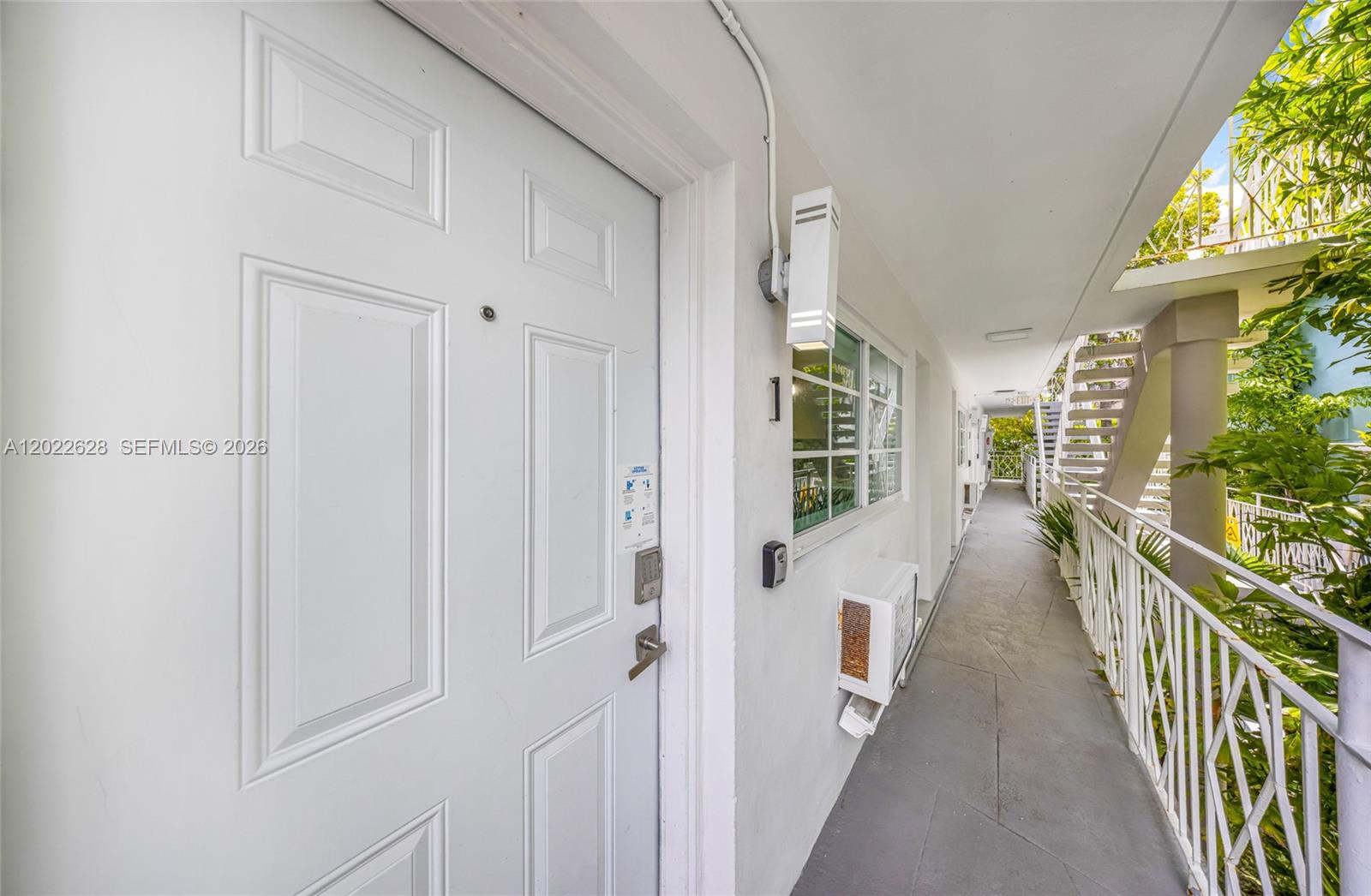A white door with a keypad lock opens onto an outdoor walkway with stairs — 7830 Abbott Ave # 25, Miami Beach FL 33141, MIAMI BEACH, FL
