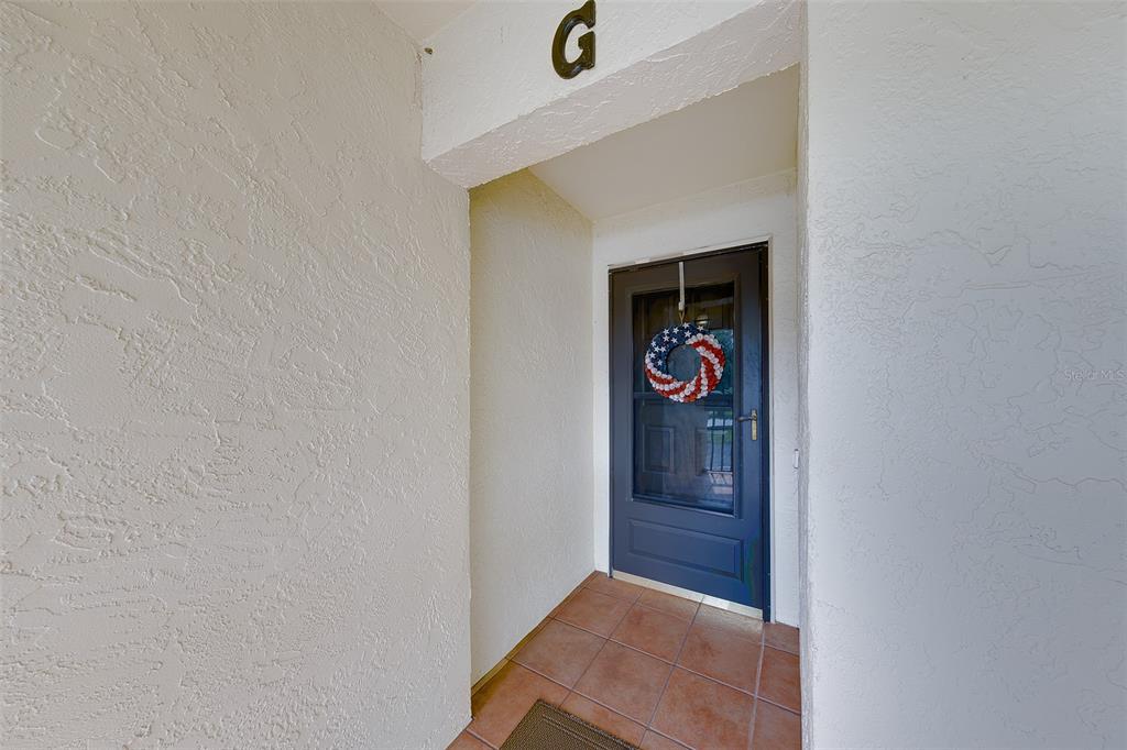 An exterior entryway features a dark door with a patriotic wreath and tiled flooring — 1801 E LAKE ROAD UNIT 20G, PALM HARBOR, FL
