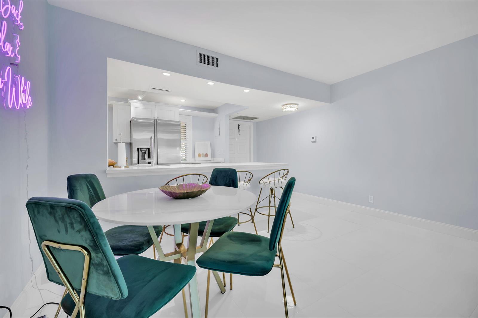 A dining area with a round table and green velvet chairs sits before a kitchen — 2800 N Palm Aire Drive # 108, Pompano Beach FL 33069, POMPANO BEACH, FL