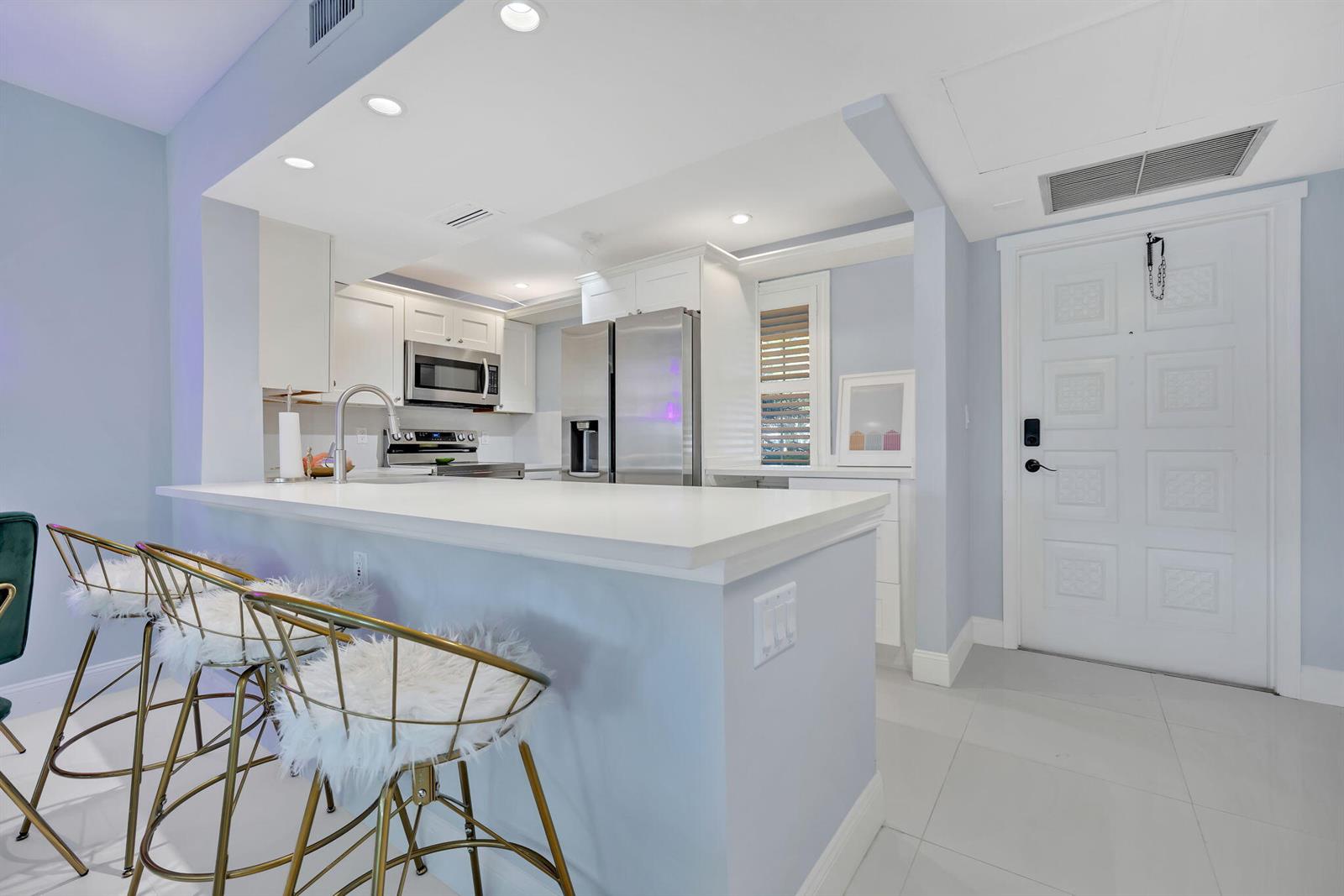 A kitchen features a white quartz breakfast bar, stainless steel appliances, and gold-framed bar stools — 2800 N Palm Aire Drive # 108, Pompano Beach FL 33069, POMPANO BEACH, FL