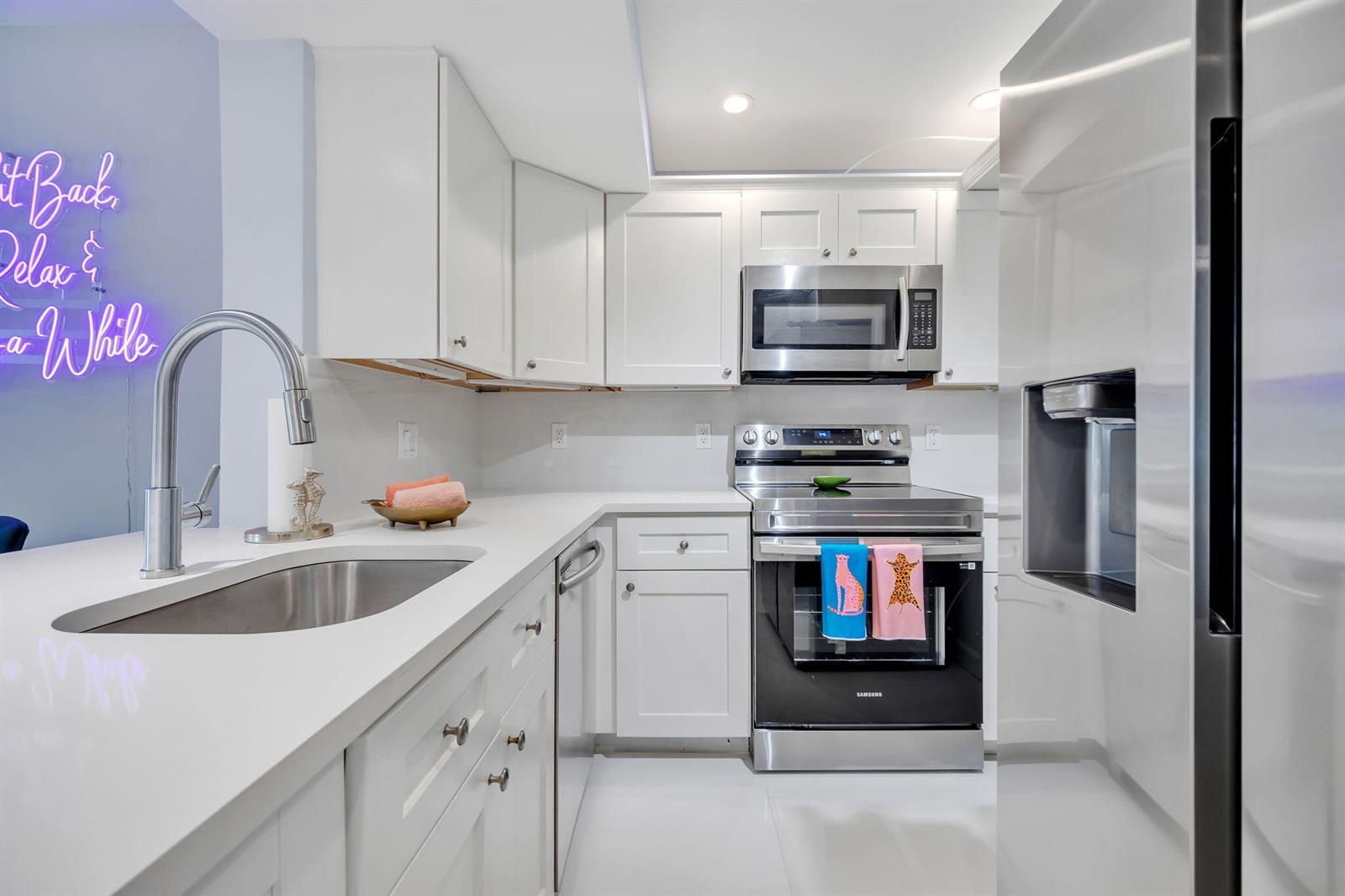 A modern kitchen features white cabinetry, stainless steel appliances, and white countertops — 2800 N Palm Aire Drive # 108, Pompano Beach FL 33069, POMPANO BEACH, FL