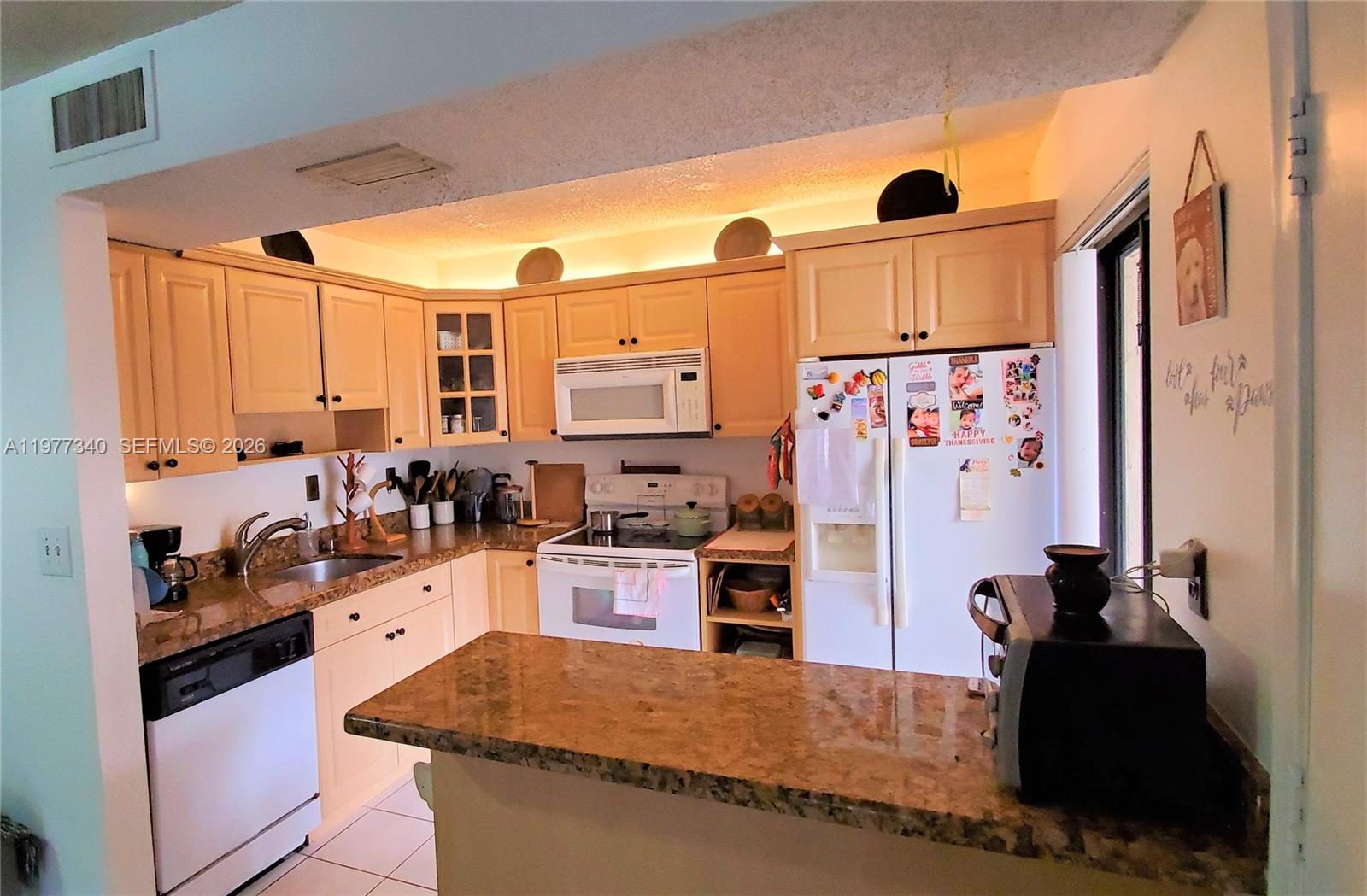 A kitchen features light wood cabinets, granite countertops, white appliances, and under-cabinet lighting — 20025 NE 3rd Ct # 1, Miami FL 33179, MIAMI, FL