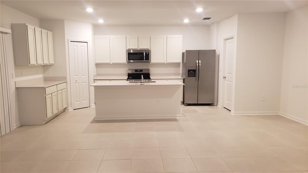 A modern kitchen features white cabinets, stainless steel appliances, a center island, and tile flooring — 3910 AMERS LOOP, HAINES CITY, FL