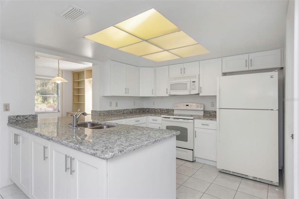 A kitchen with white cabinets, granite countertops, a central island, and a white refrigerator — 2024 HEATHFIELD CIRCLE UNIT 155, SUN CITY CENTER, FL