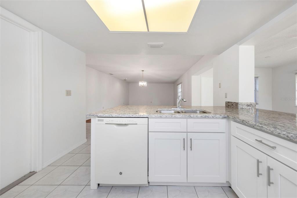 A kitchen island with a white dishwasher, white cabinets, and granite countertops — 2024 HEATHFIELD CIRCLE UNIT 155, SUN CITY CENTER, FL