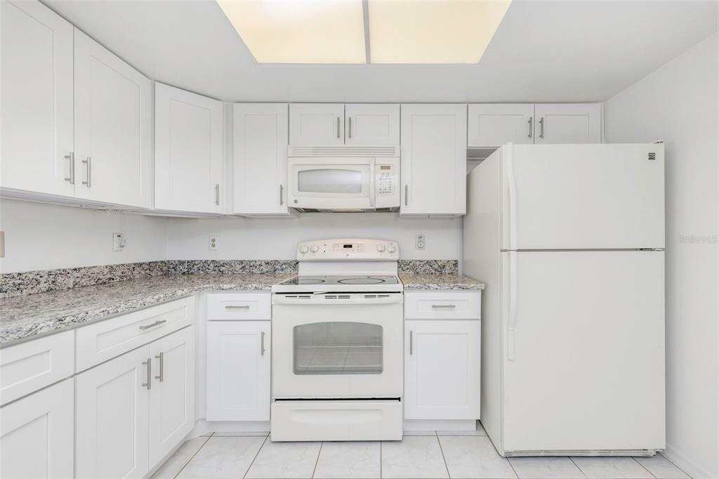 A kitchen with white cabinets, white appliances, and speckled granite countertops — 2024 HEATHFIELD CIRCLE UNIT 155, SUN CITY CENTER, FL