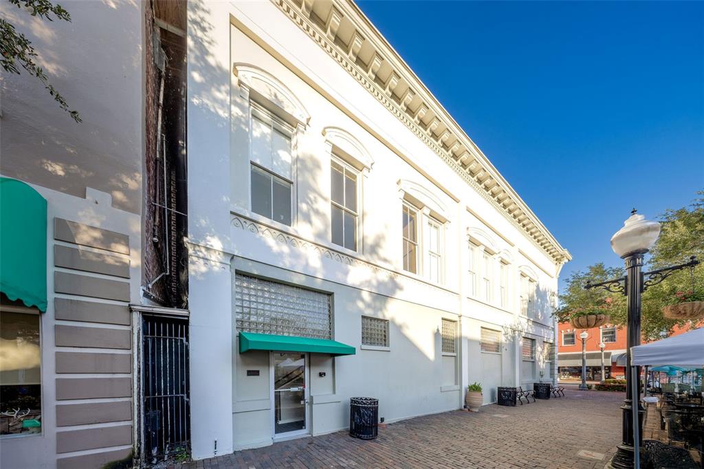 A white two-story commercial building with arched windows and a green awning on a brick plaza — 121 E 1ST STREET UNIT 101, SANFORD, FL