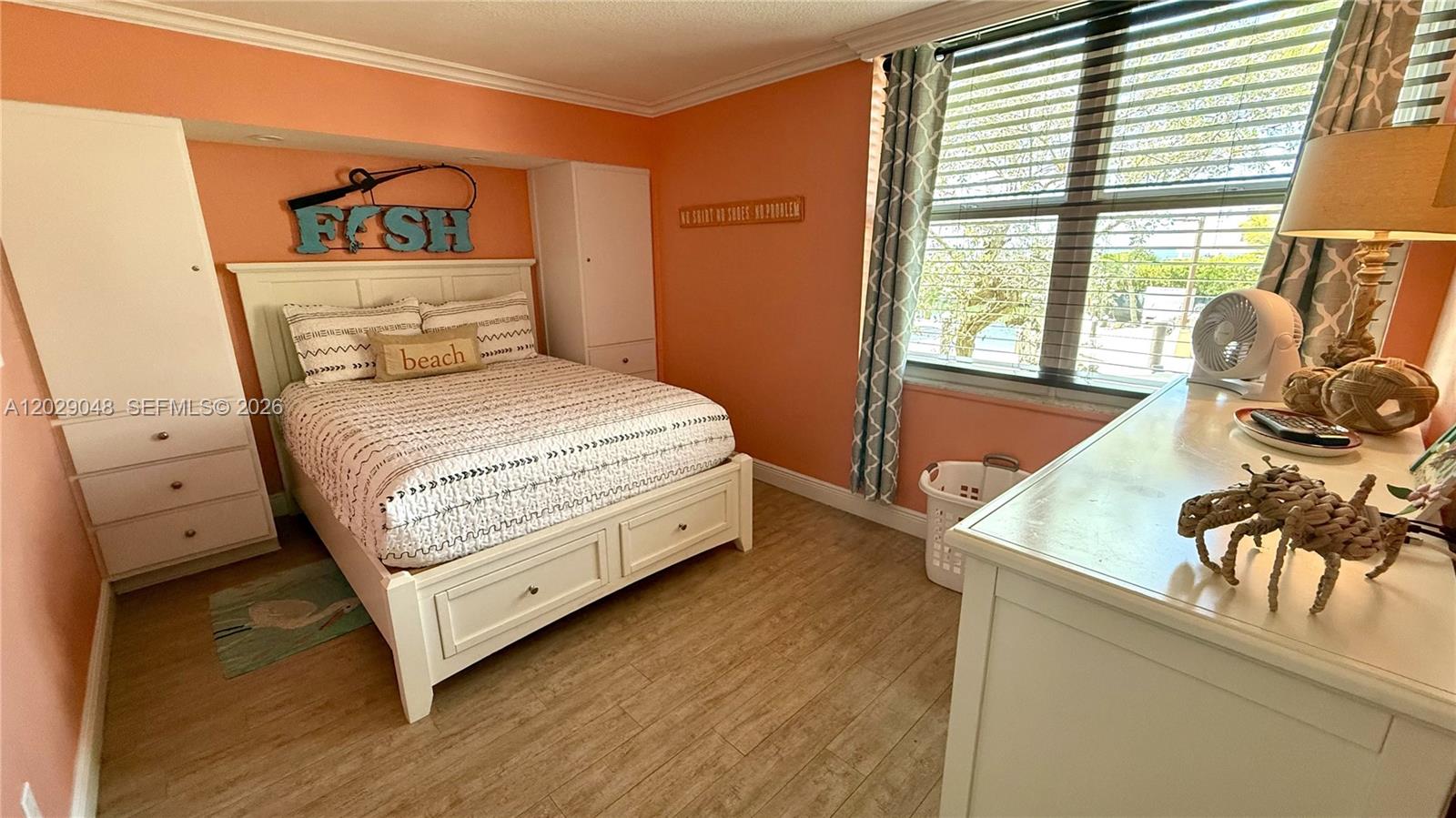 A bedroom features a bed with beach-themed decor, light wood flooring, and peach-colored walls — 88500 overseas hwy # 108, Tavernier FL 33070, TAVERNIER, FL