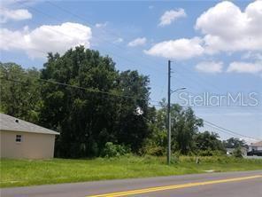 A grassy vacant lot sits next to a house under a blue sky with clouds — 204 RONTUNDA DRIVE, KISSIMMEE, FL