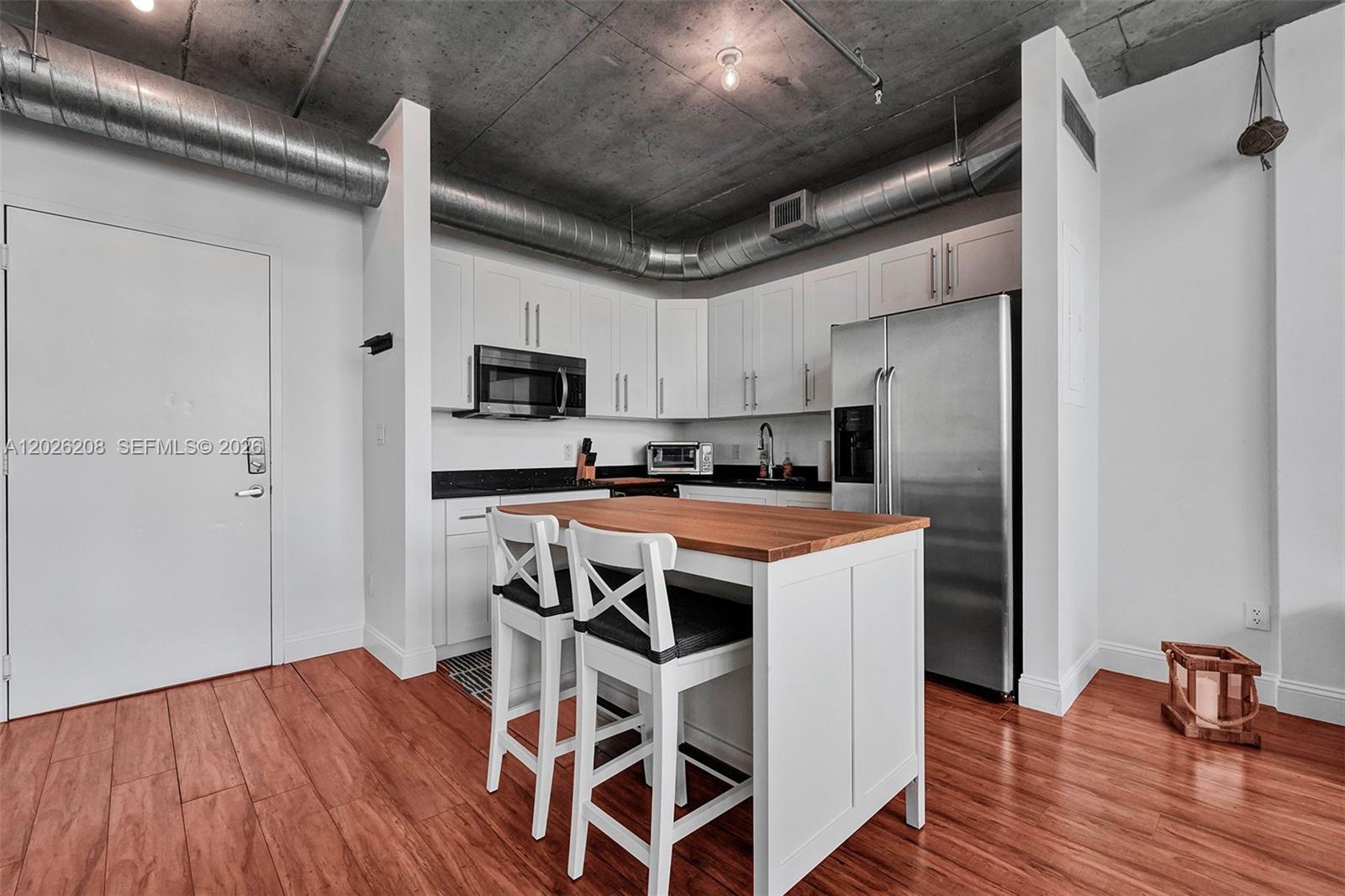 A kitchen features white cabinets, stainless steel appliances, a wooden island, and exposed ceiling ductwork — 690 SW 1st Ct, Miami FL 33130, MIAMI, FL