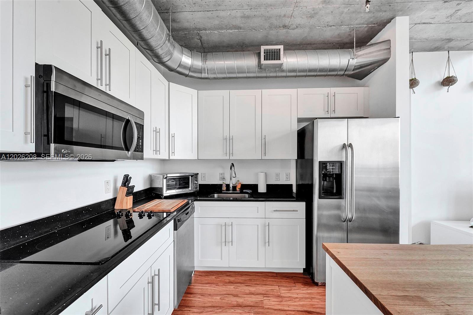 A modern kitchen features white cabinets, black countertops, stainless steel appliances, and exposed ductwork — 690 SW 1st Ct, Miami FL 33130, MIAMI, FL