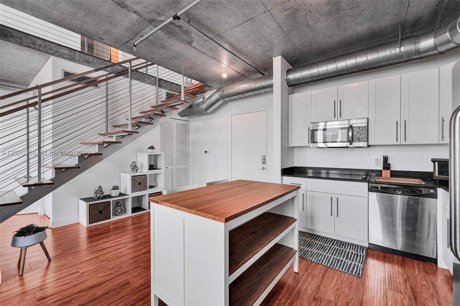 A kitchen with white cabinets, a wooden island, and a staircase under a concrete ceiling — 690 SW 1st Ct, Miami FL 33130, MIAMI, FL