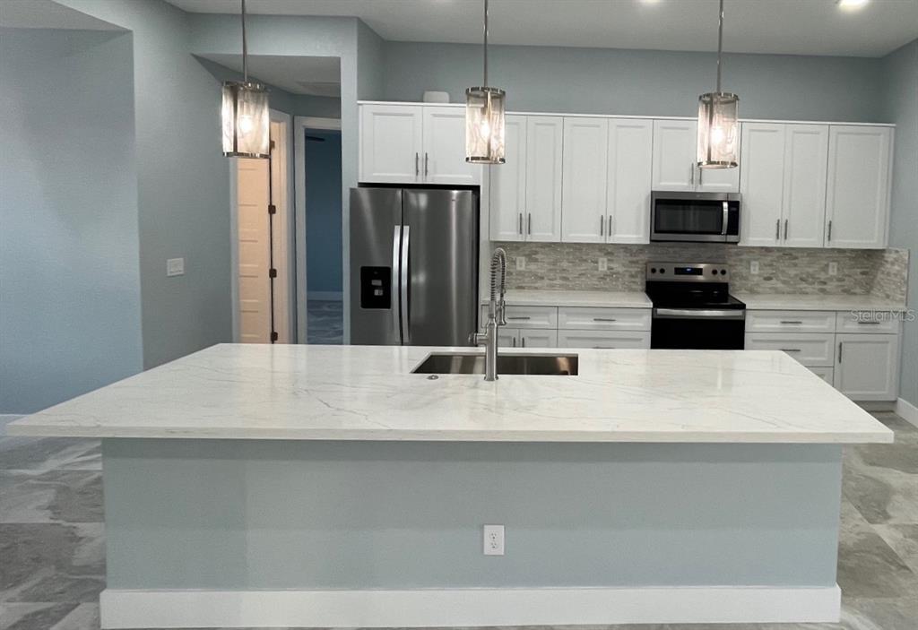 A modern kitchen features a large white quartz island, stainless steel appliances, and white cabinetry — 13342 COMMONWEALTH AVENUE, PORT CHARLOTTE, FL