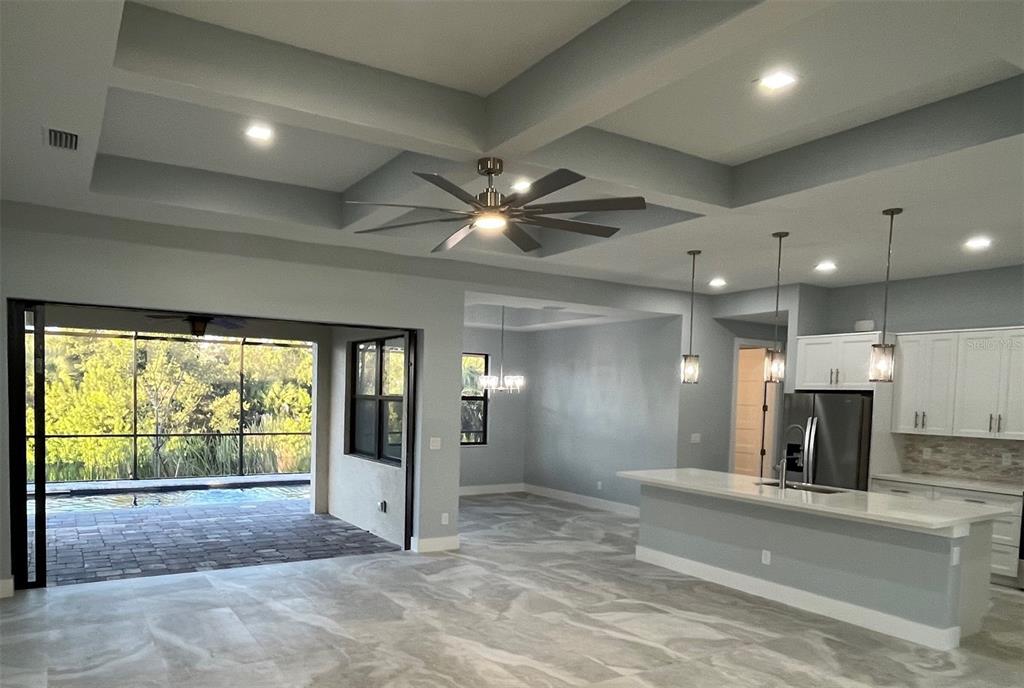 An open-concept living area features a tray ceiling, tile flooring, and a sliding door to a pool — 13342 COMMONWEALTH AVENUE, PORT CHARLOTTE, FL