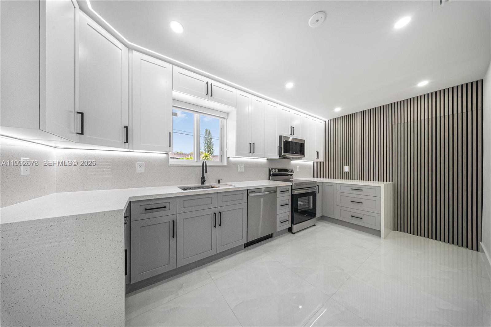 A modern kitchen features white upper cabinets, gray lower cabinets, and a wood-slat accent wall — 17860 SW 110th Ct, Miami FL 33157, MIAMI, FL