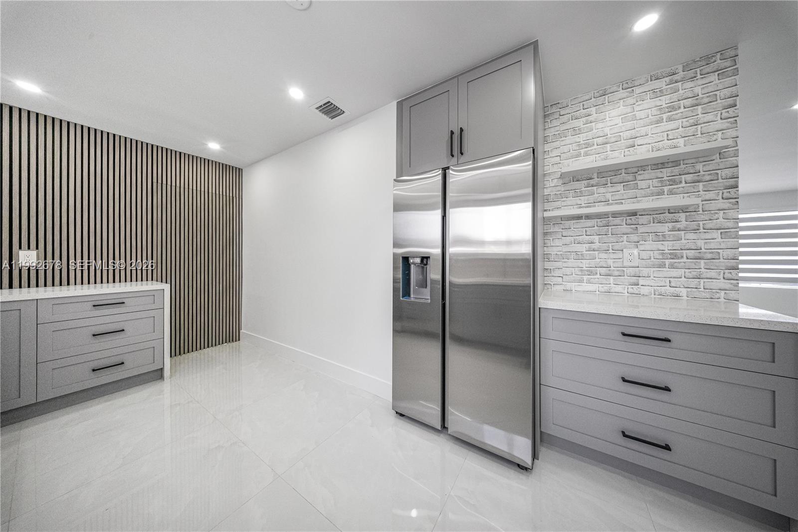 A modern kitchen features gray cabinetry, stainless steel appliances, and a white brick accent wall — 17860 SW 110th Ct, Miami FL 33157, MIAMI, FL